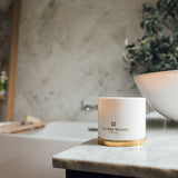A lit Melissa Wilkes England scented candle is displayed  in a gorgeous modern bathroom. The candle is sat on its lid which acts as coaster. The scent this Pomelo Bitters gives is amazing. It will transport you to a warm summers evening. 
